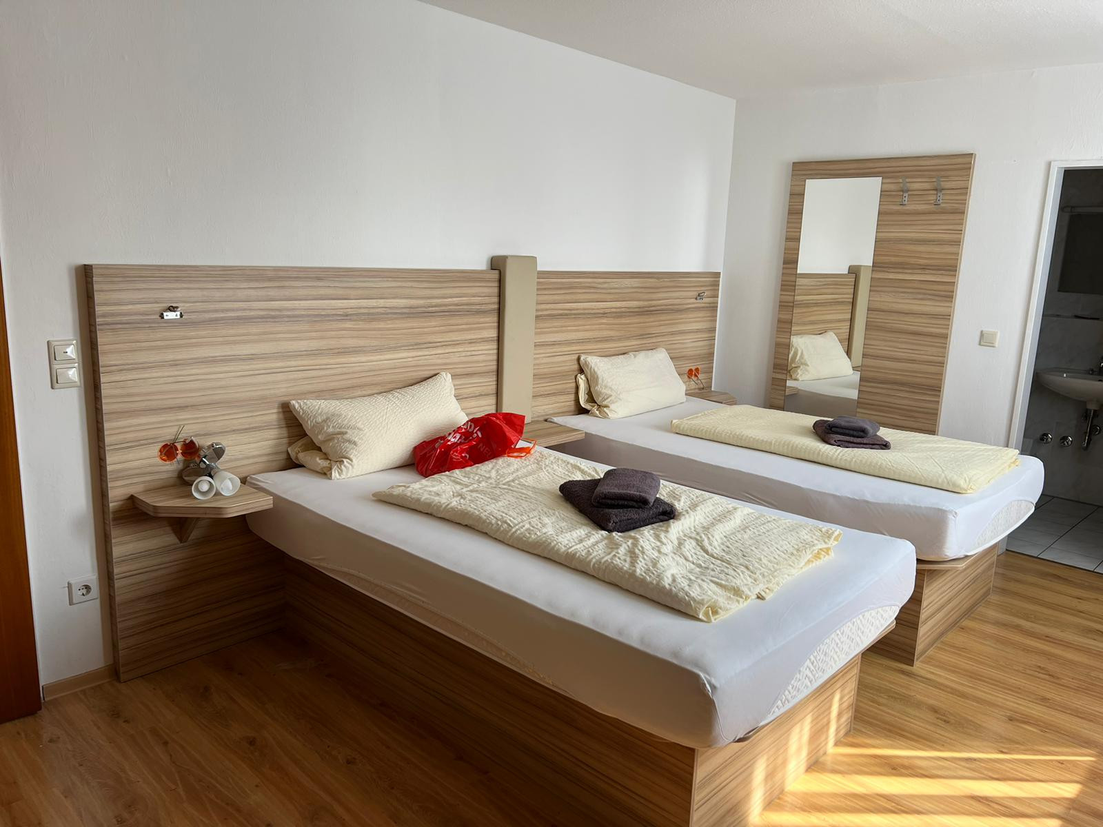 Gästezimmer mit zwei Betten, maßgefertigten Holz-Kopfteilen, Spiegel und angrenzendem Bad.